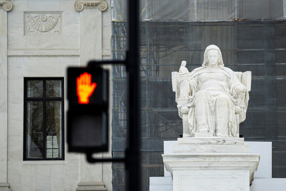 The Contemplation of Justice statue outside the US Supreme Court beside a "Don't Walk" upraised hand symbol in Washington, D.C.