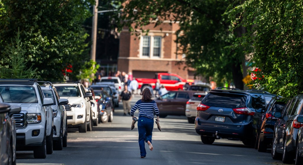 A woman holds her shoes and runs past haphazardly parked cars toward Annunciation Church.