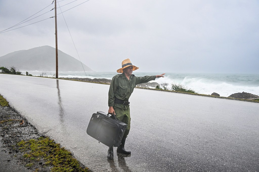 A man with a suitcase holds out his hand to hitch a ride in the rain.
