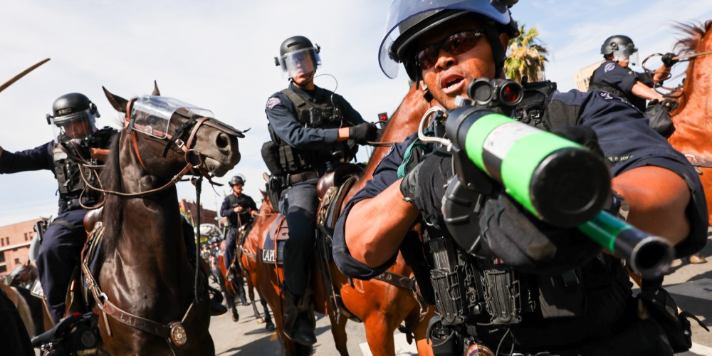 A police officer holds a weapon to the camera as protesters face off with police outside of a federal building in downtown Los Angeles for an anti-Trump "No Kings Day" demonstration.