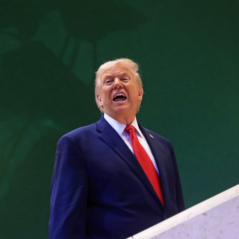 Donald Trump against a green wall, with his mouth open.