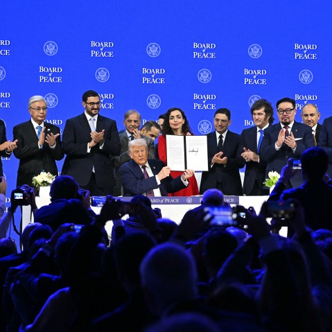 Presidents, prime ministers, and other leaders from around the world surround Donald Trump, who holds a signed charter. Audience members in the foreground take pictures.