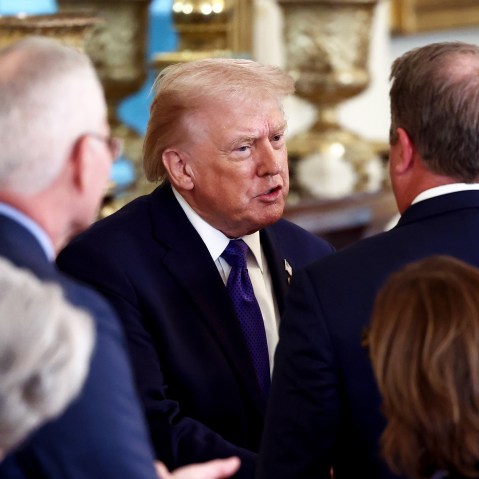 President Donald Trump speaks with people who have their back turned toward the camera.