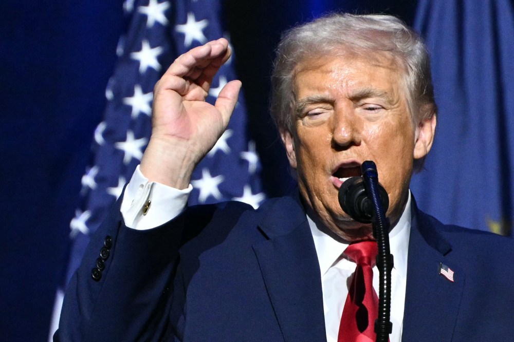 Donald Trump in front of a microphone with his arm raised.
