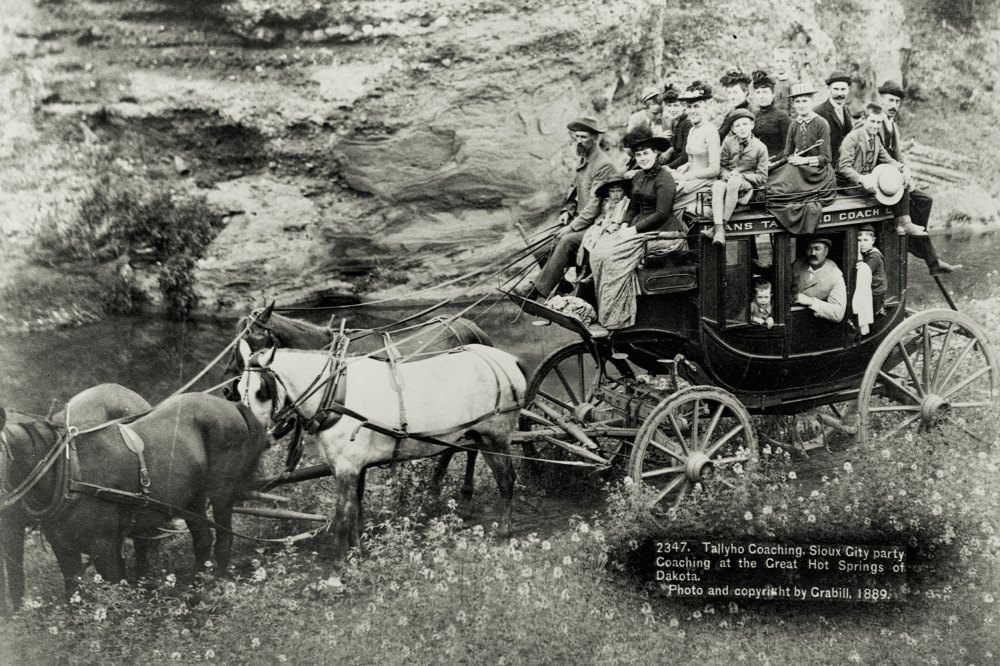 A large group of people ride in and on top of a stagecoach, Hot Springs, South Dakota, 1889.