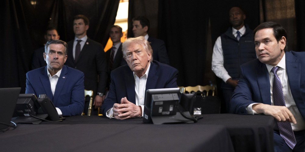 President Donald Trump, center, sits with his hands folded.