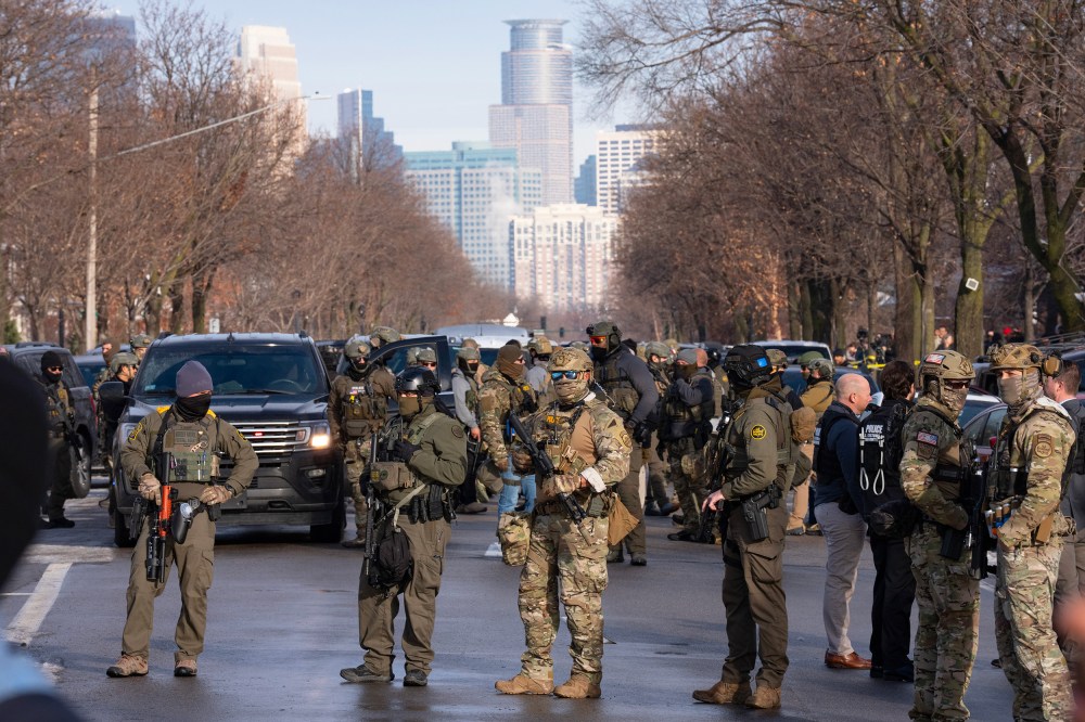 Federal agents stand in the street with the a partial view of the Minneapolis skyline in the background.
