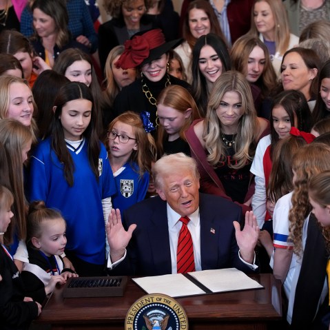 President Trump surrounded by female athletes of varying ages signs an executive order.