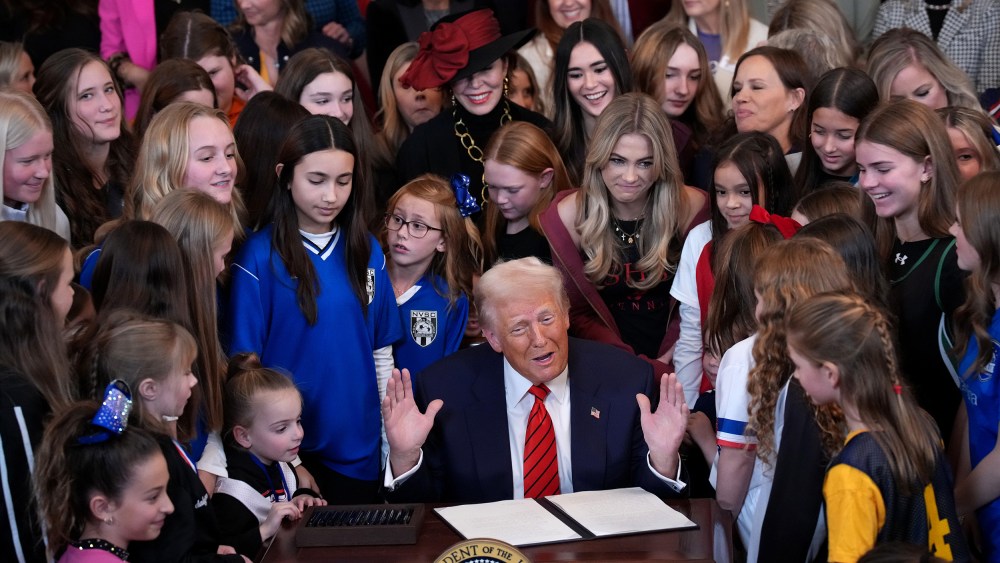 President Trump surrounded by female athletes of varying ages signs an executive order.