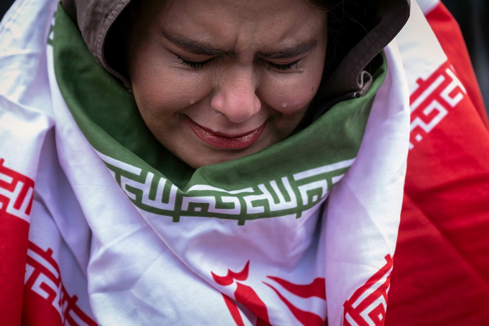 A young woman, wrapped in an Iranian flag, cries.