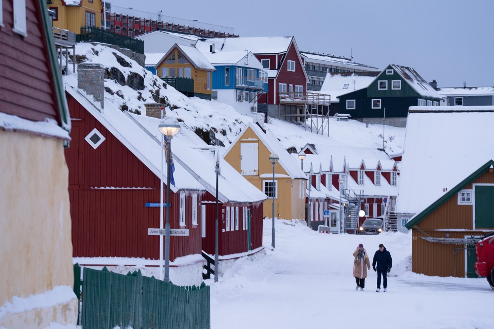 Two people walk among brightly painted houses in the snow.