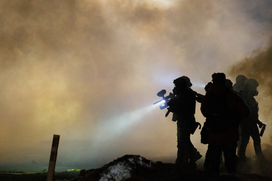 Federal agents walk in the cloud of tear gas wearing tactical gear, including gas masks.
