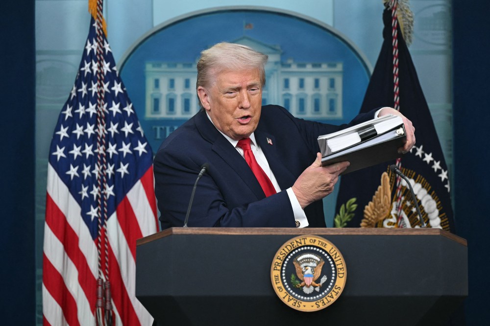 President Trump holds up a folder of documents as he speaks to the media during a briefing.