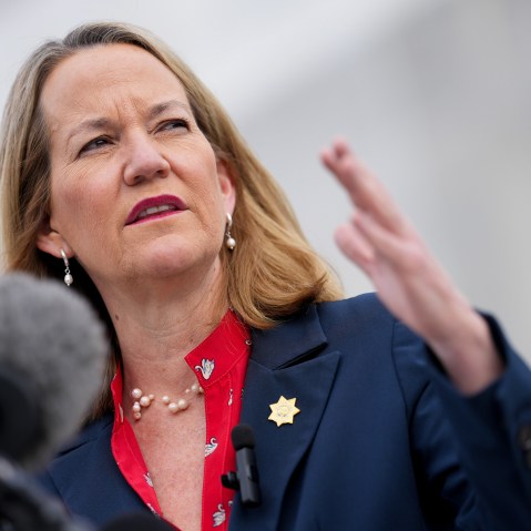 Kris Mayes gestures in front of a microphone.