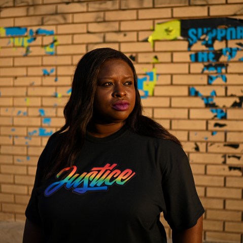 Nekima Levy Armstrong, wearing a shirt that says "justice" in rainbow letters, poses in front of a brick wall.