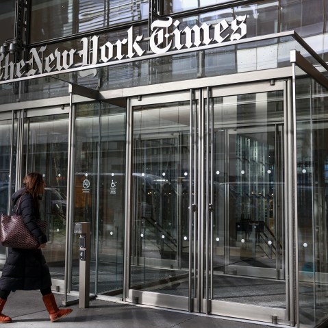 A woman walks into the New York Times building where we can fully see the building sign in the frame.
