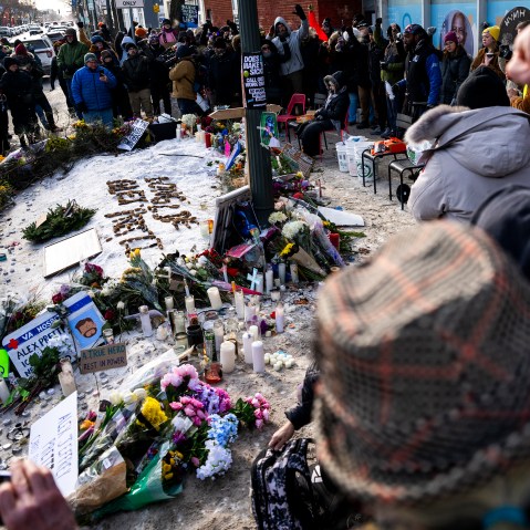 People stand around a memorial created on the ground for Alex Pretti.