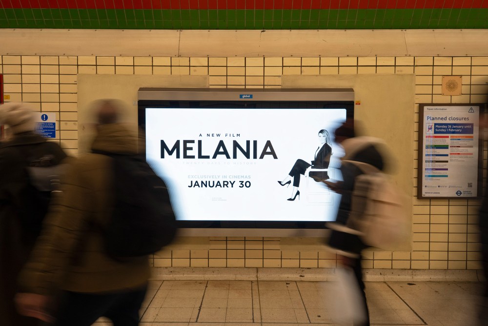 People, blurred in motion, walk past an advertisement for the movie "Melania."