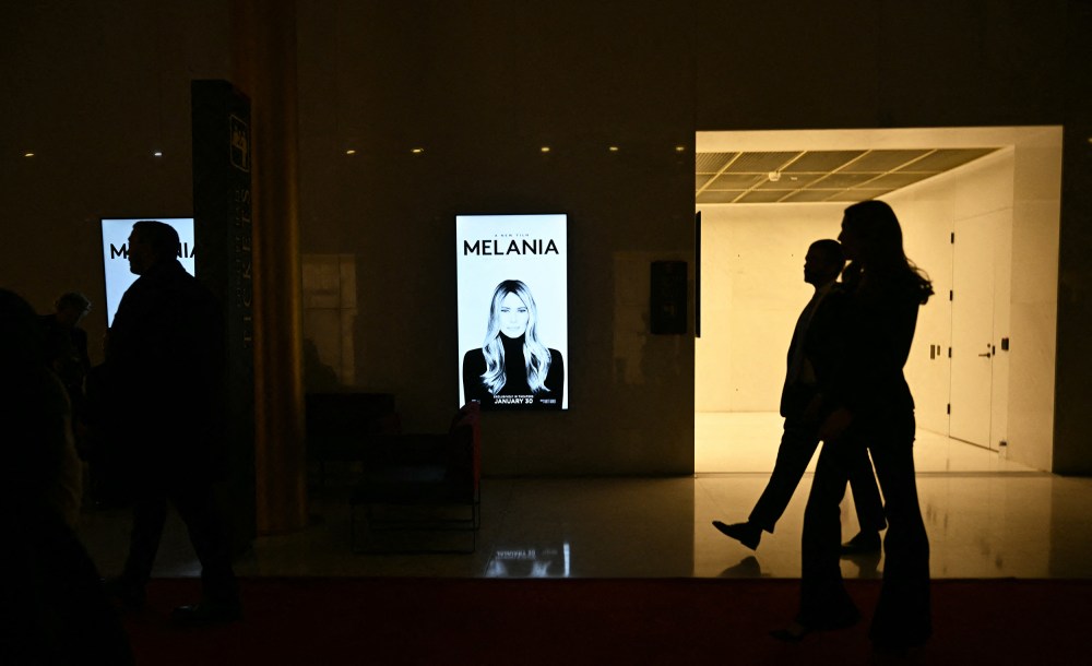 Silhouettes walk past a poster for "Melania."