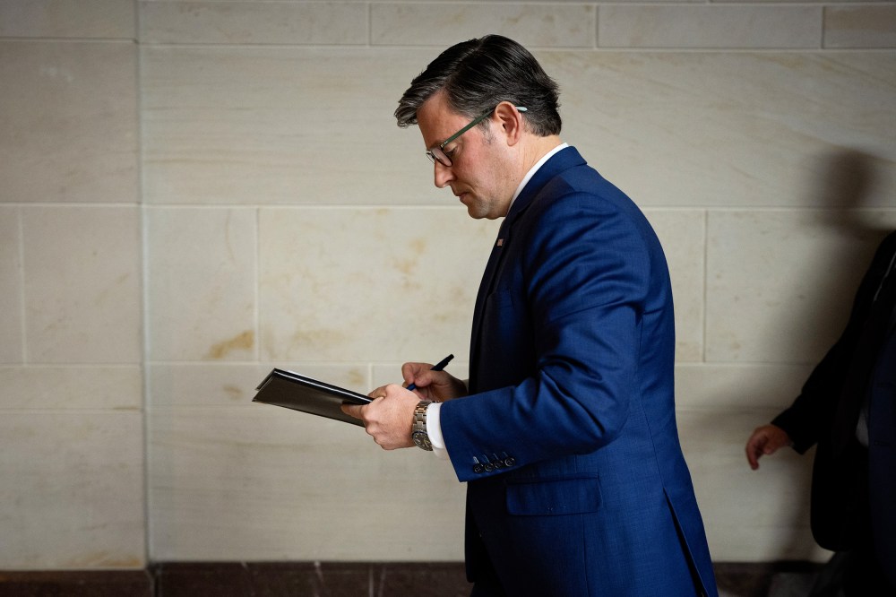 Mike Johnson, facing left, walks while writing on a piece of paper.