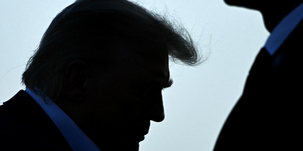Trump's profile is seen as he walks up to the place. A security person stands on the right side.