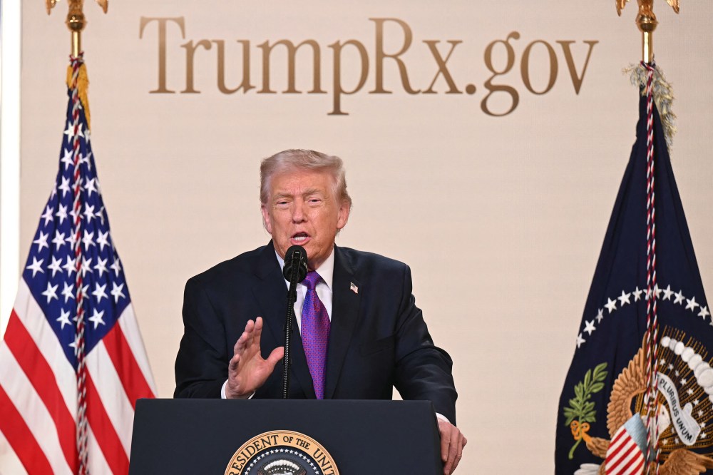 Donald Trump speaks into a microphone at a podium. The website "TrumpRx.gov" is on the wall behind him.