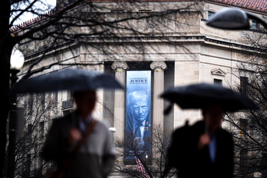 Two pedestrians holding umbrellas walk past the DOJ hq.