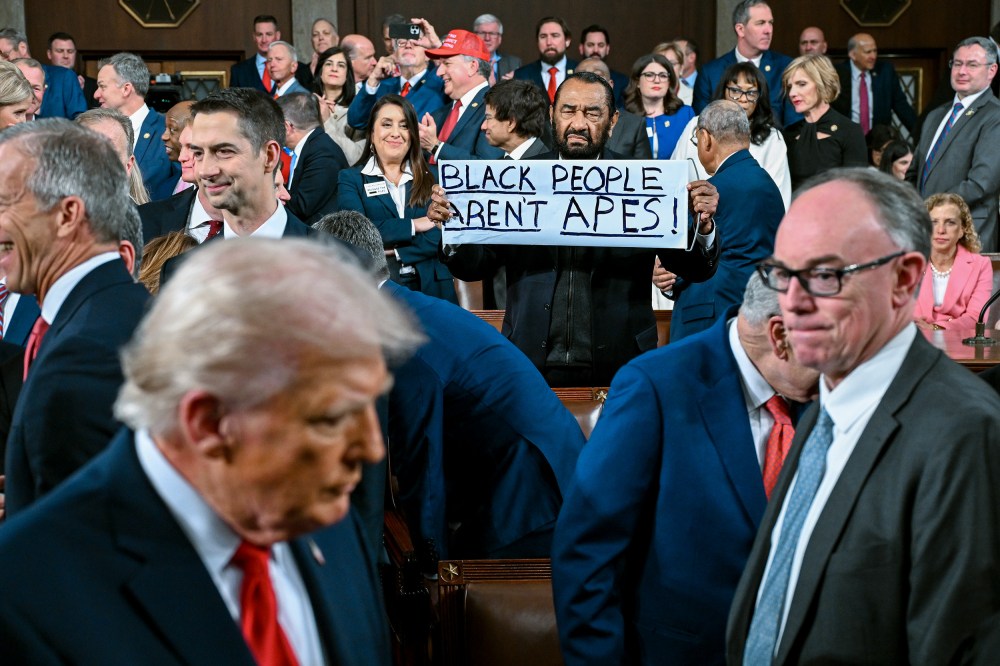 Al Green holds a sign that says "Black People Aren't Apes!" In the foreground, President Trump is visible but out of focus.