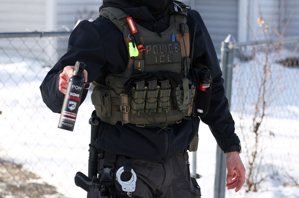 Torso of an ICE agent is seen as he aims a pepper spray canister forward.