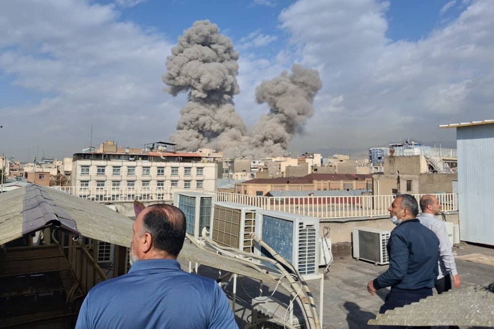Men standing on rooftops look on at clouds of smoke rise from US airstrikes