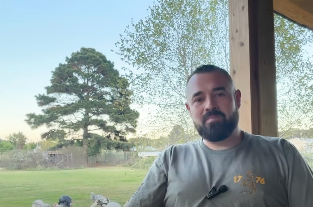 Aaron Spencer sits at a porch as he speaks. Turkeys can be seen in the background.