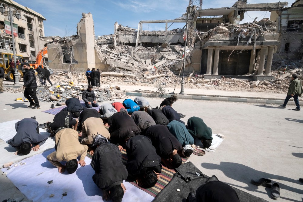 Men put their faces on the ground as they pray outside the ruins of a building.