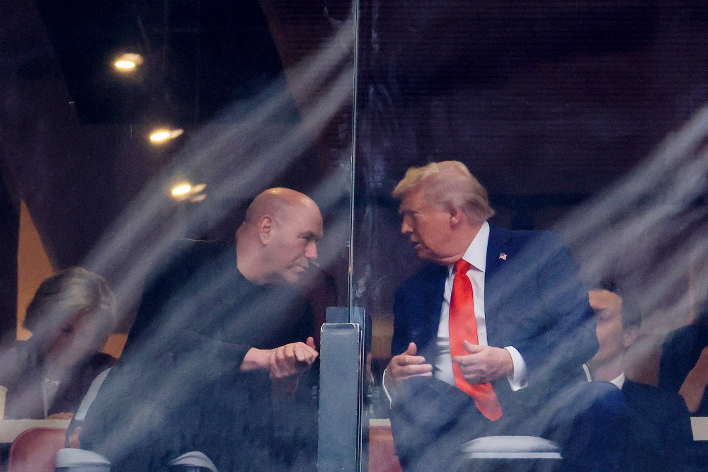 Dana White leans over to Donald Trump as they chat seen behind a plastic panel.