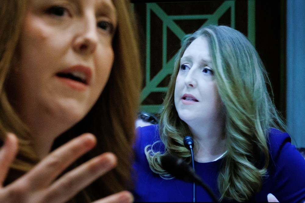 Casey Means in seen out of focus on the left side of the frame while her face is shown on a screen on the right - in focus.