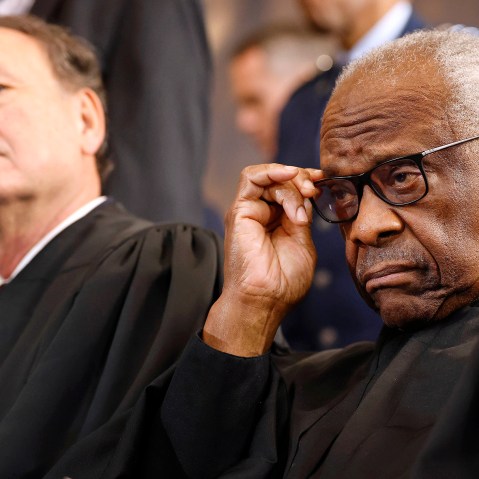 Clarence Thomas adjusts his glasses as Samuel Alito leans back in the background.
