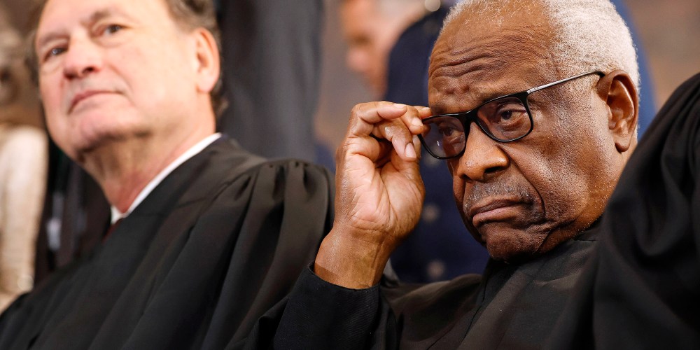 Clarence Thomas adjusts his glasses as Samuel Alito leans back in the background.