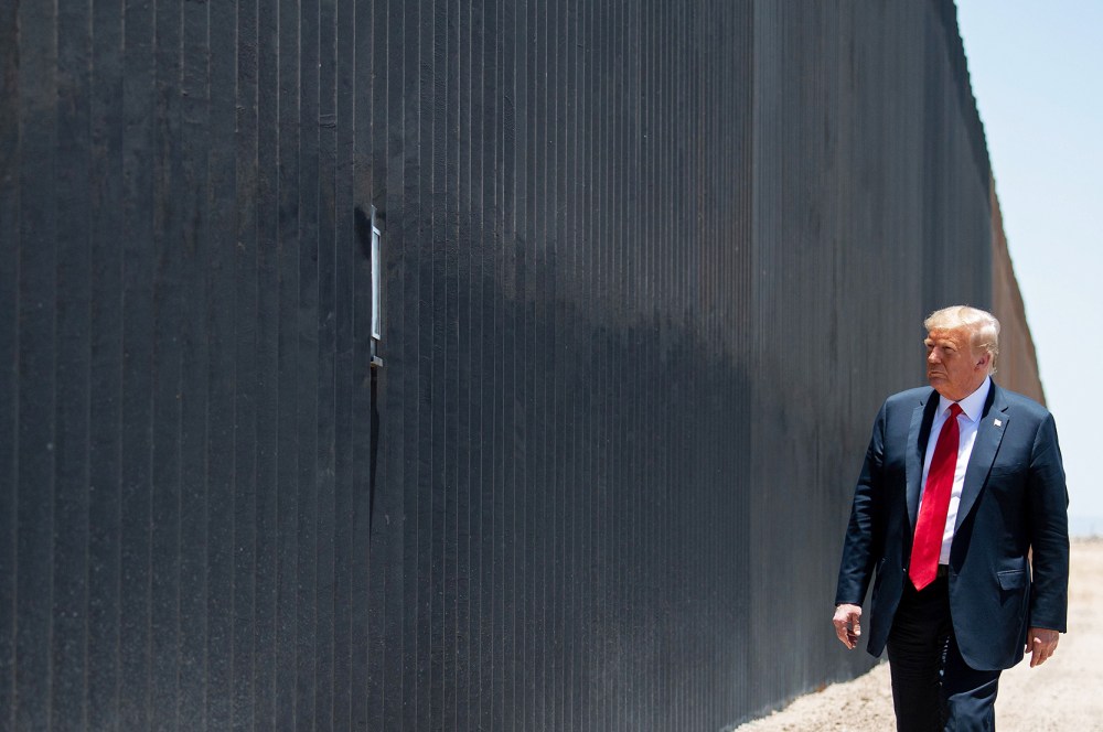 Donald Trump stands in front of a border wall.