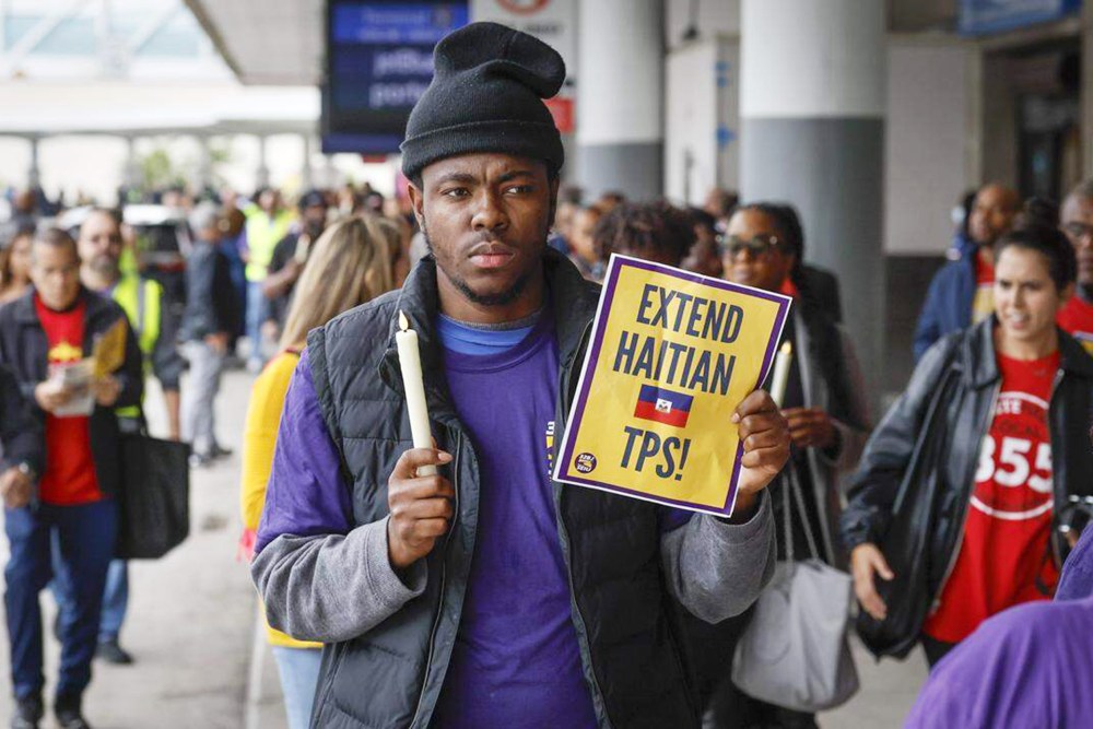 A man holds a candle and a sign about [protection tps for Haitians.