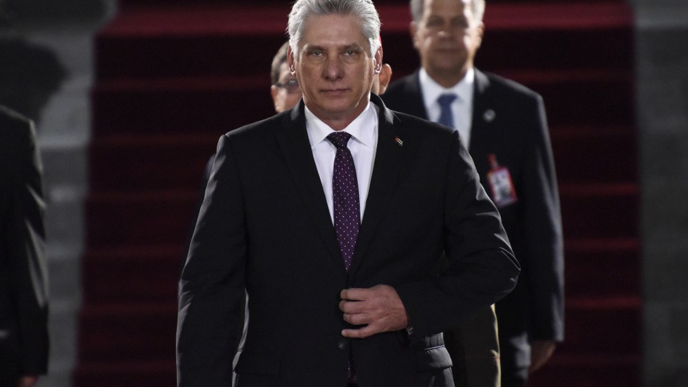 Miguel Díaz-Canel walks toward the camera with his hand on his suit jacket's button.