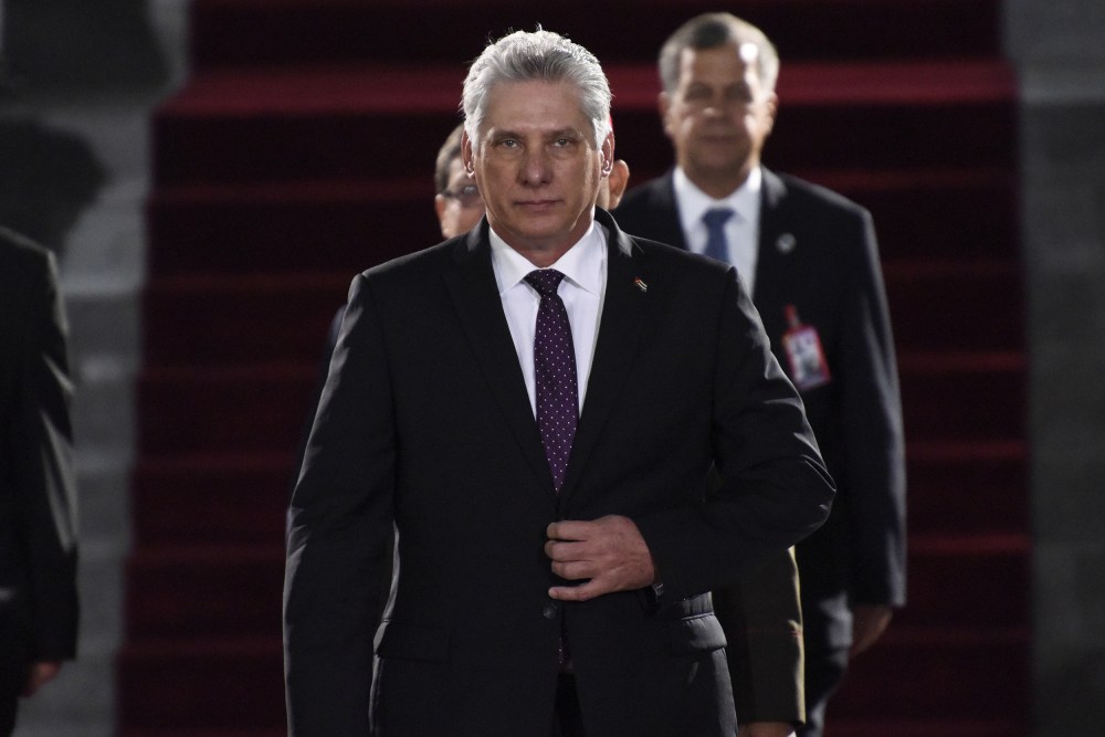 Miguel Díaz-Canel walks toward the camera with his hand on his suit jacket's button.