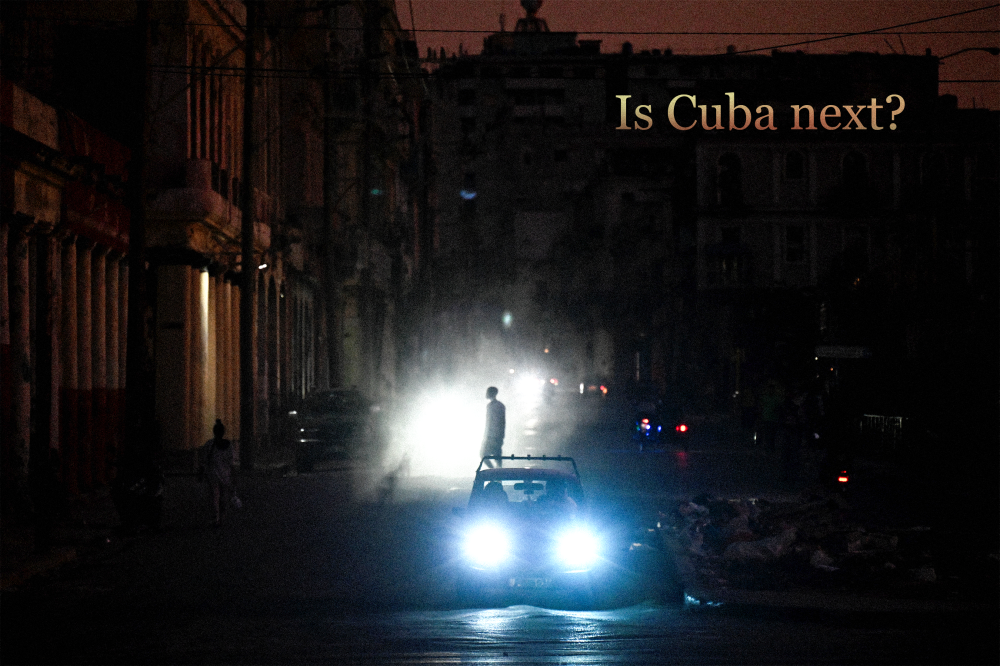 A man walks while cars cruise along a street during a blackout in Havana, Cuba. Text on top right reads “Is Cuba Next?”